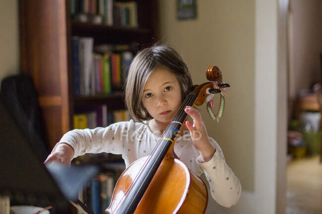 A serious little girl practices cello in beautiful light at home — Stock Photo
