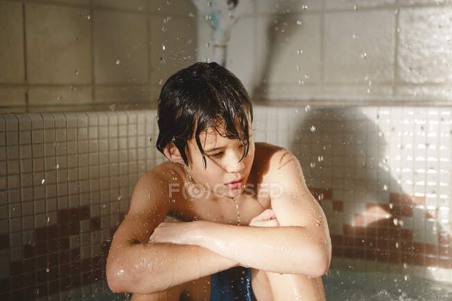 Un bel ragazzo si siede in una piscina con gocce d'acqua che cadono intorno a lui — Foto stock