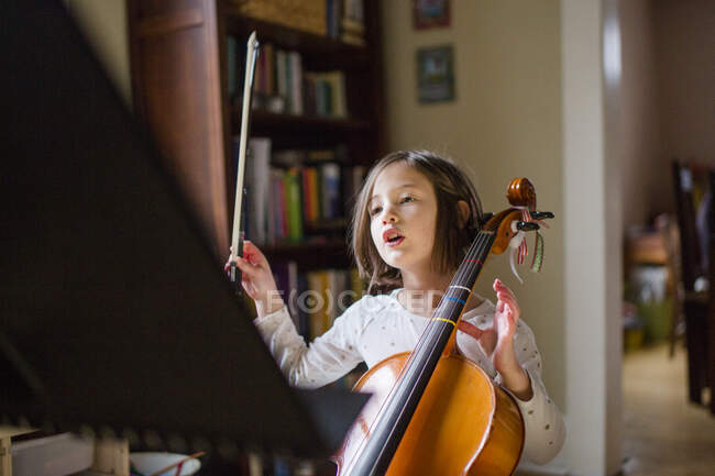 Una niña sosteniendo violonchelo levanta su arco en preparación para tocar - foto de stock
