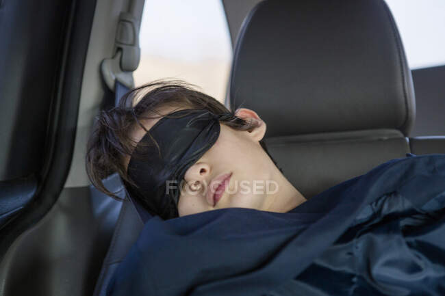 Ребенок спит в автомобильном кресле в маске для глаз, покрытой одеялом — стоковое фото