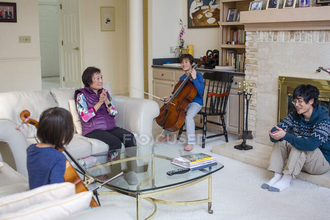 Dos niños tocan el violonchelo mientras la abuela y el padre aplauden - foto de stock