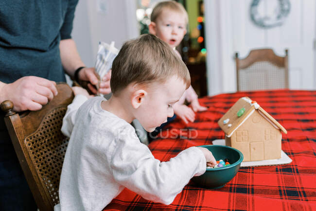 Two children decorating a gingerbread house at the dinner table — Stock Photo