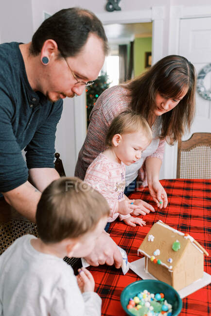 Familie mit kleinen Kindern dekoriert im Dezember ein Lebkuchenhaus — Stockfoto