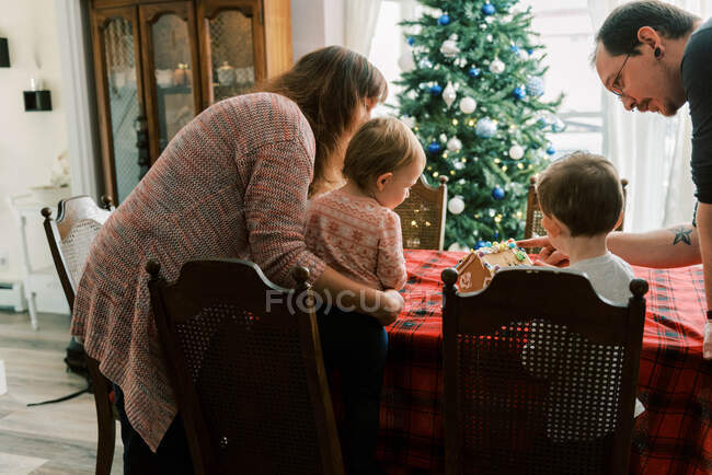 Сім'я з маленькими дітьми прикрашає імбирний будинок у грудні — стокове фото