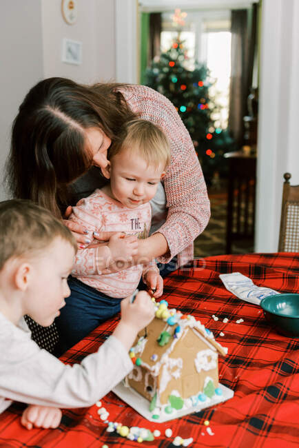 A mother and her children making a gingerbread house for the holidays — Stock Photo