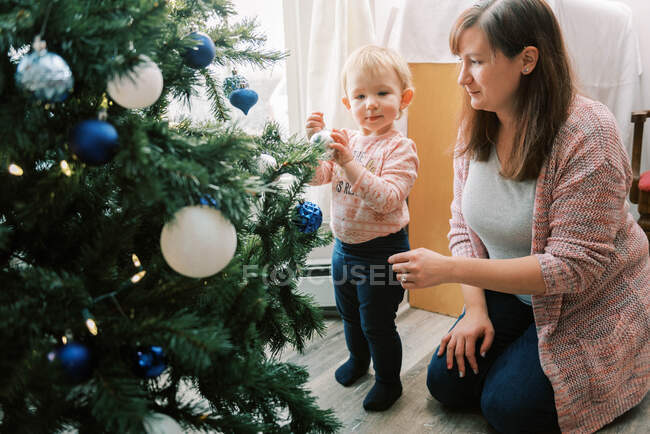 Pequeña niña niña madre decorando árbol de Navidad juntos - foto de stock