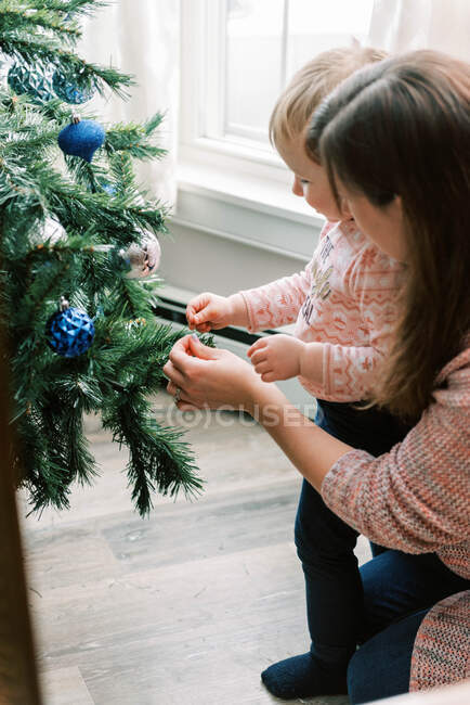 Pequeño niño y su madre poniendo adornos en el árbol de Navidad - foto de stock