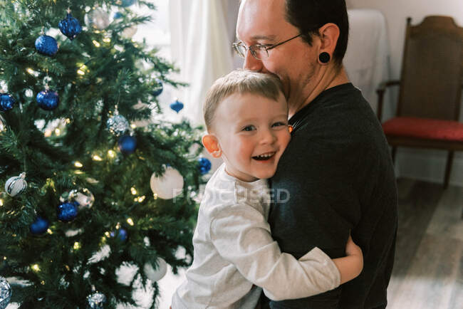 A father and son hugging and laughing by Christmas tree in living room — Stock Photo