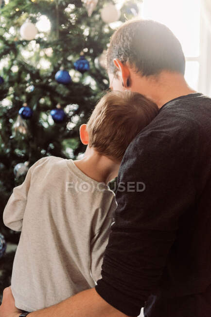 Отец и малыш обнимаются у рождественской елки, делясь нежным моментом — стоковое фото