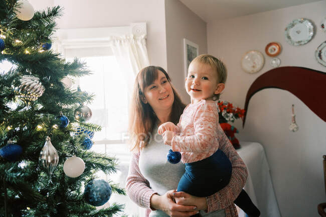 Familia con niños pequeños decorando un árbol de Navidad en diciembre - foto de stock