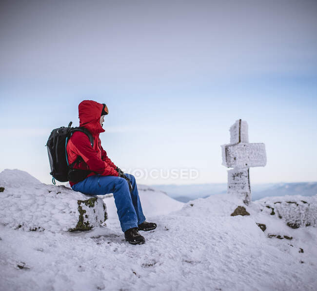 Winter hiker sits on snow covered rock with snowy sign in cold. — Stock Photo