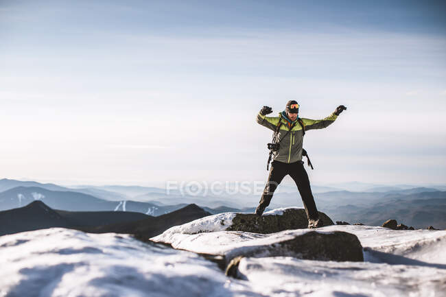 Man with camera jumps from icy rock on mountain summit in winter — Stock Photo