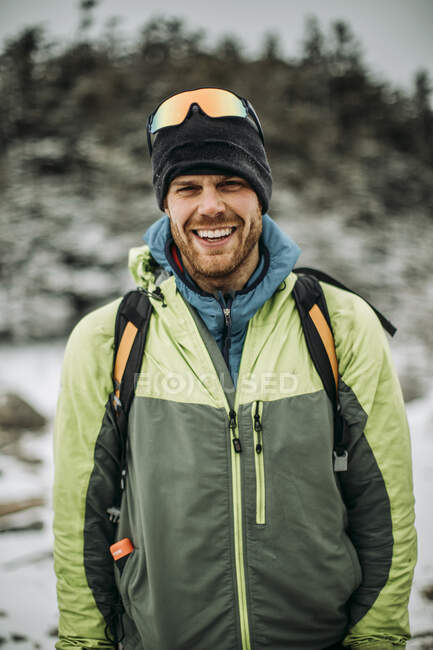 Portrait of smiling man in winter jacket and hat wearing backpack — Stock Photo