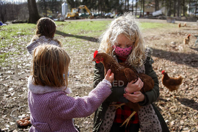 Mädchen mit blonden Haaren hält Hühner auf einem Bauernhof — Stockfoto