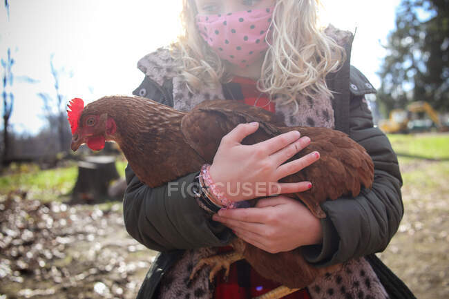 Close up of girl wearing a mask holding chicken on a farm — Stock Photo
