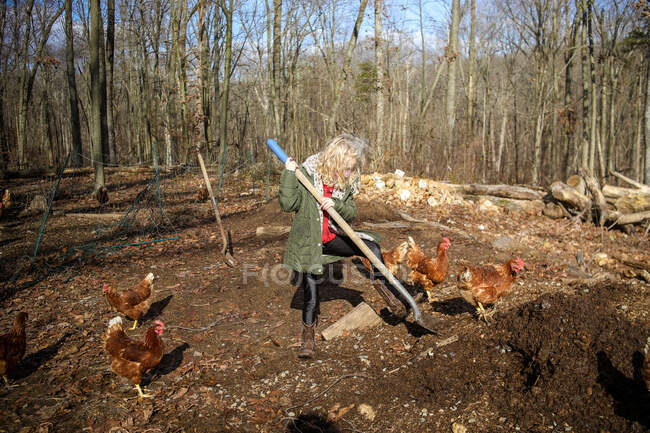 Mädchen mit blonden Haaren gräbt mit Schaufel auf Bauernhof mit Hühnern — Stockfoto