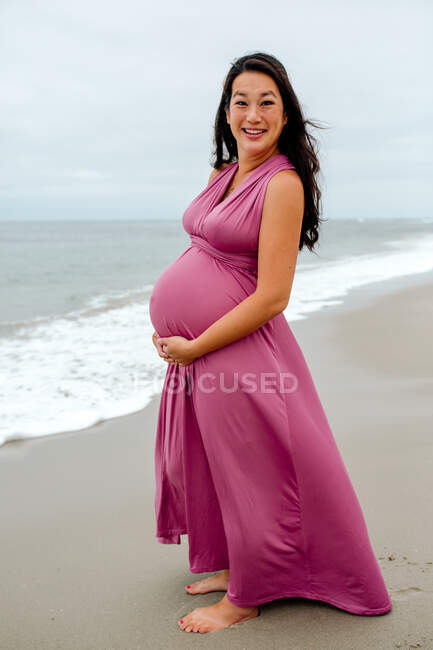 Muito grávida sorrindo mulher asiática em vestido rosa na praia — Fotografia de Stock