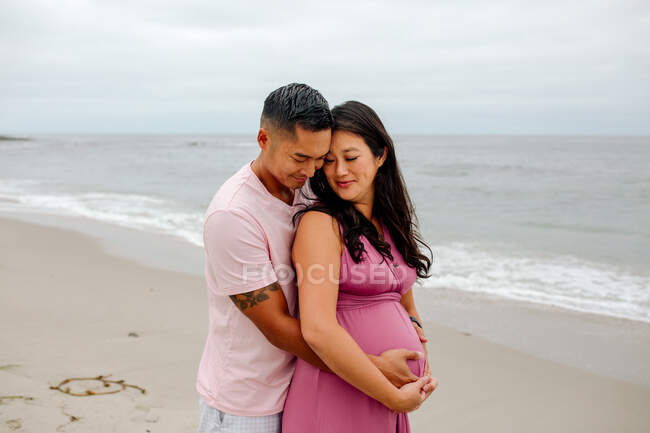 Loving husband embraces pregnant wife from behind at the ocean — Stock Photo