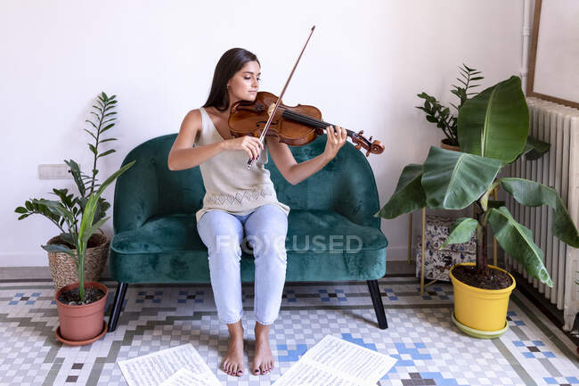 Ragazza seduta a suonare la viola, spartiti che circondano i suoi piedi nudi — Foto stock