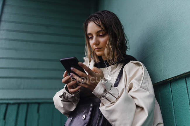 Mujer encogida con teléfonos, cerca de una pared verde - foto de stock