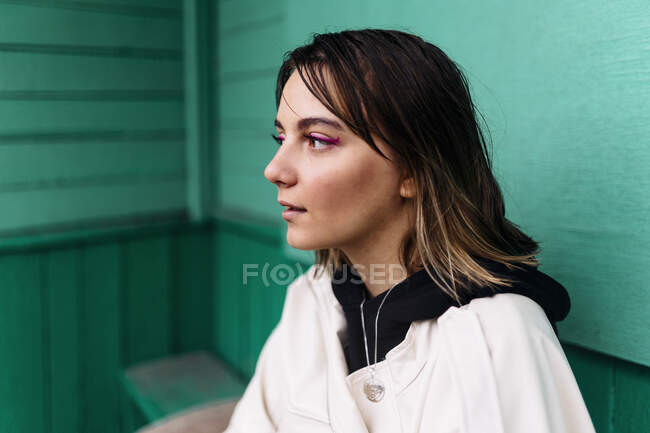 Donna sorpresa seduta vicino a un muro verde in una giacca bianca — Foto stock