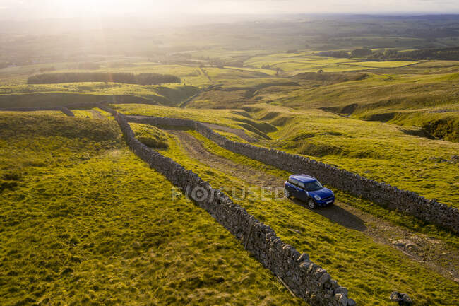Carro dirigindo estrada rural inglesa com vista para colinas — Fotografia de Stock