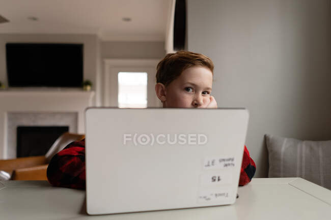 Young redhead boy looking bored over laptop computer indoors at table — Stock Photo