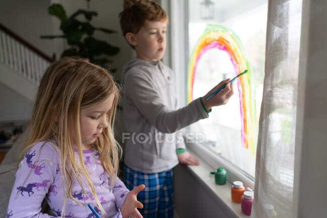 Kids painting rainbow on window in house — Stock Photo