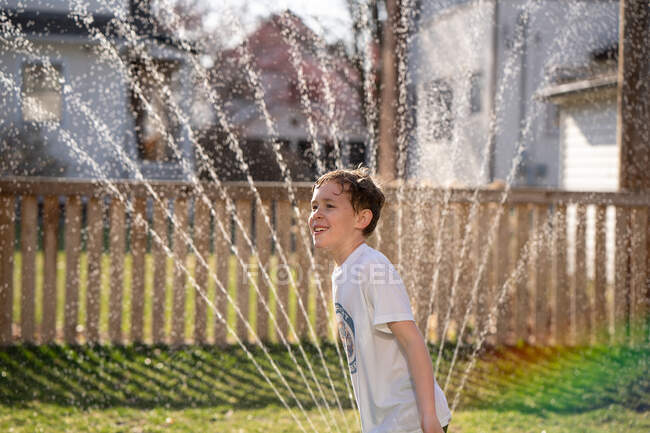 Мальчик играет в разбрызгиватель воды на заднем дворе — стоковое фото