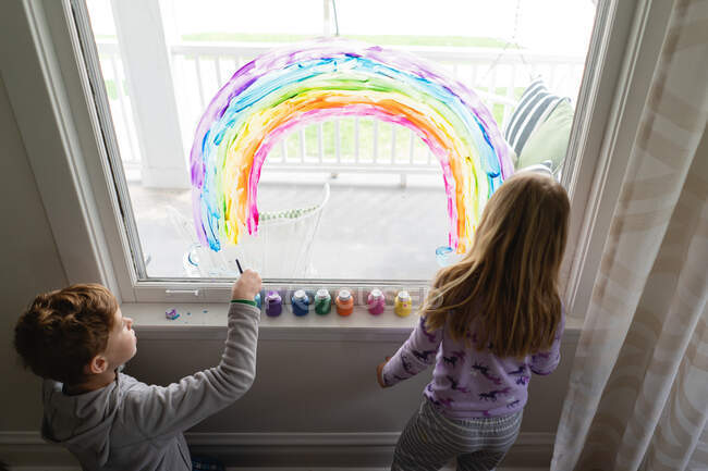 Top down view of siblings painting rainbow on living room window — Stock Photo
