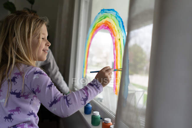 Вид збоку усміхненої дівчини, що малює веселку на вікні — стокове фото