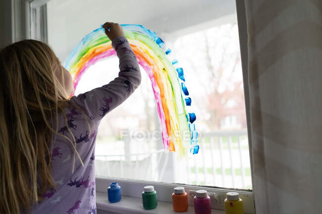 Back view of blond girl painting rainbow on window — Stock Photo
