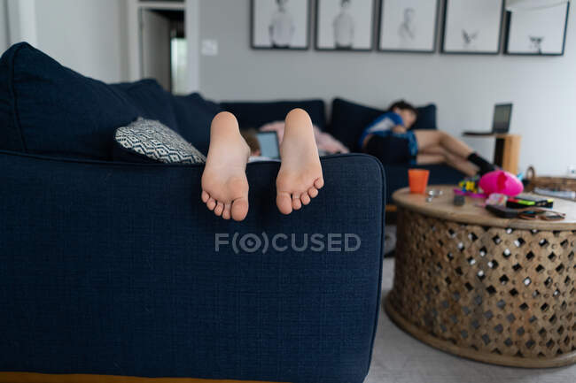 Ноги и пальцы ребенка, лежащего на диване с братом на заднем плане — стоковое фото