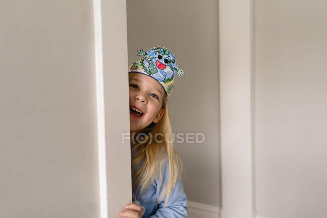 Sorridente citar menina com terra dia headband espreitando em torno da parede — Fotografia de Stock