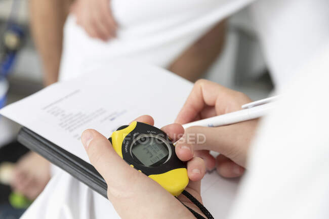 Close-up of female hand holding clipboard with pen and stopwatch — Stock Photo
