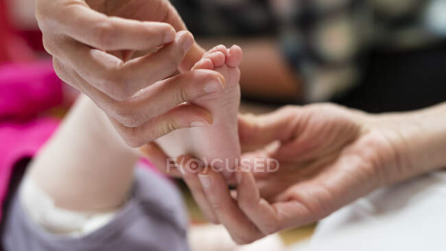 Inyección recortada de médico examinando los pies del bebé - foto de stock