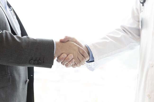 Schnappschuss von Geschäftsmann und Arzt im weißen Kittel beim Händeschütteln — Stockfoto