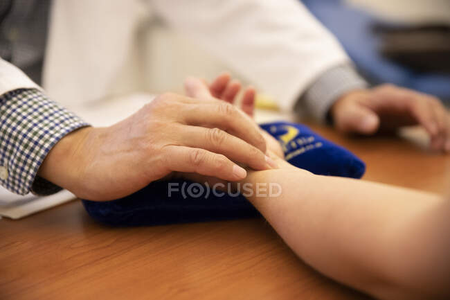 Inyección recortada del médico que mide la frecuencia cardíaca del paciente infantil - foto de stock