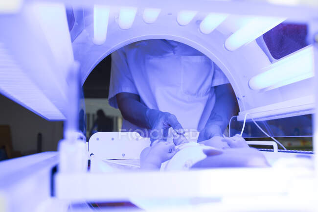 Primer plano del médico femenino examinando al bebé recién nacido bajo luz ultravioleta - foto de stock