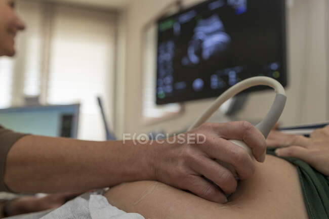 Primer plano del médico examinando el vientre de la mujer embarazada con ultrasonido - foto de stock