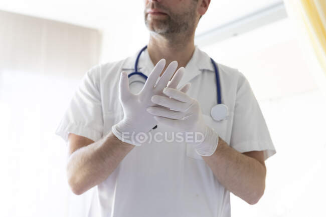 Hombre en uniforme médico blanco con guantes de goma - foto de stock
