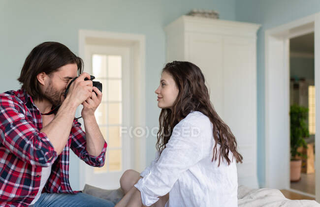 Young male shooting female on bed while resting at home in weekend together — Stock Photo