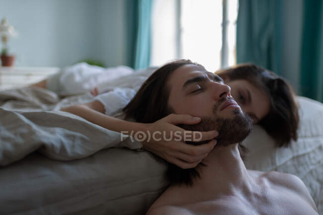 Junge Frau ruht auf Bett und berührt Bart ihres Freundes mit geschlossenen Augen zu Hause — Stockfoto