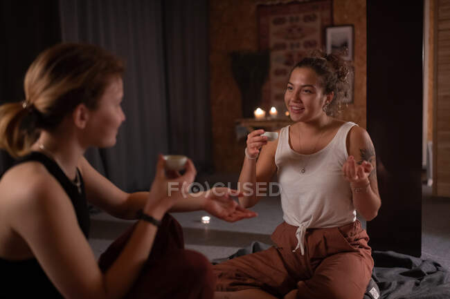 Glad female teacher and student drinking tea and speaking after yoga session — Stock Photo