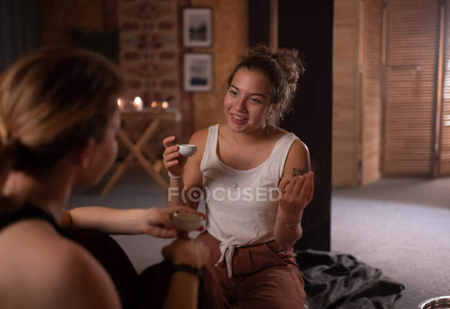 Mujer feliz con taza de té sonriendo y hablando con el profesor de yoga durante la hora del té - foto de stock