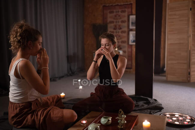 Mujeres jóvenes bebiendo té asiático con los ojos cerrados durante el té en el estudio de yoga - foto de stock