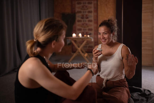 Young female with Asian tea smiling and telling joke to tutor in yoga studio — Stock Photo