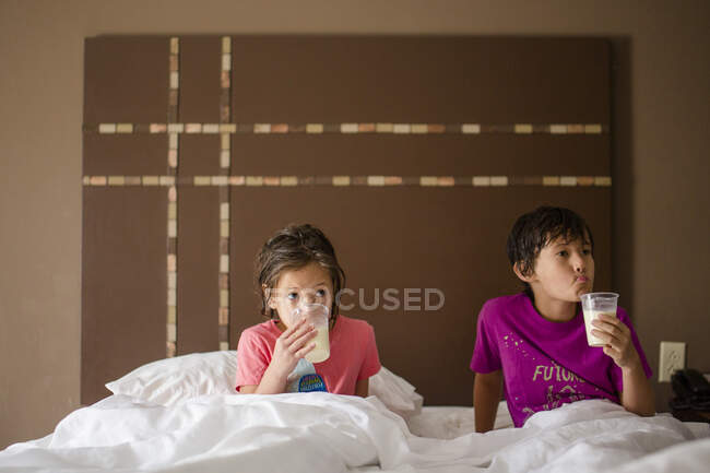 Двоє маленьких дітей лежали разом у королівському ліжку, випиваючи чашки молока — стокове фото