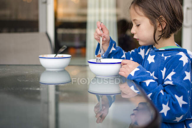 A small girl reflected in glass table eats breakfast outside — Stock Photo
