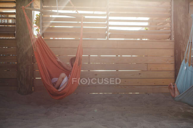 Crianças pequenas relaxam em redes coloridas na praia em luz dourada — Fotografia de Stock